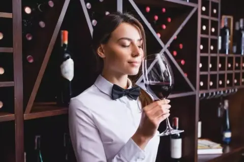 Sommelier annusa un bicchiere di vino Cannaiola, circondata da scaffali pieni di bottiglie.