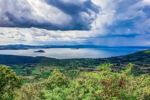 Vista panoramica del lago di Bolsena con isole, colline verdi e un cielo drammatico. Un paesaggio mozzafiato da Capodimonte.