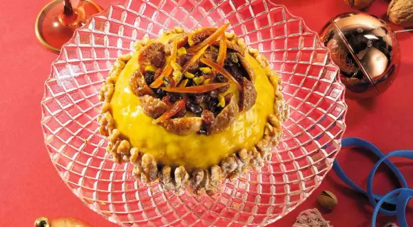 Pangialli ricetta: dolce giallo decorato con frutta secca e scorze d'arancia, circondato da noci su un piatto di cristallo.