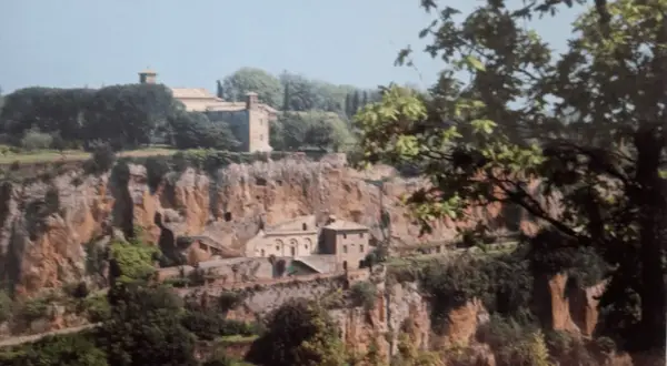Antico complesso monastico di Santa Maria ad Rupes, incastonato nella roccia, con edifici in pietra e vegetazione rigogliosa.