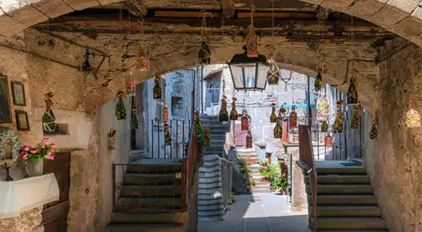 Un vicolo suggestivo a Vitorchiano, Viterbo, con bottiglie decorate appese e un'icona sacra.