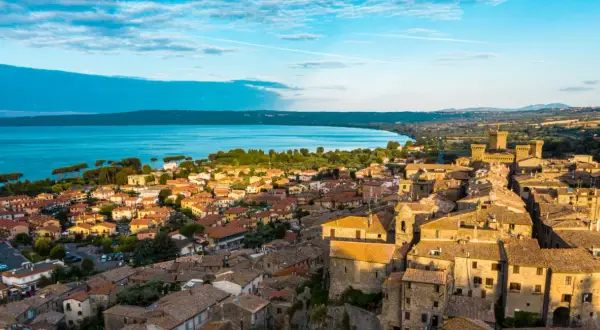 Borghi da visitare vicino Bolsena: vista aerea di un antico castello e case con tetti in tegole rosse, con il lago sullo sfondo.