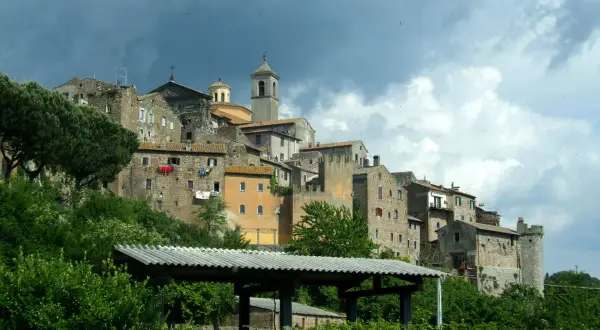 Antico borgo di **Tuscie Vetralla**, con case in pietra aggrappate alla collina sotto un cielo nuvoloso.