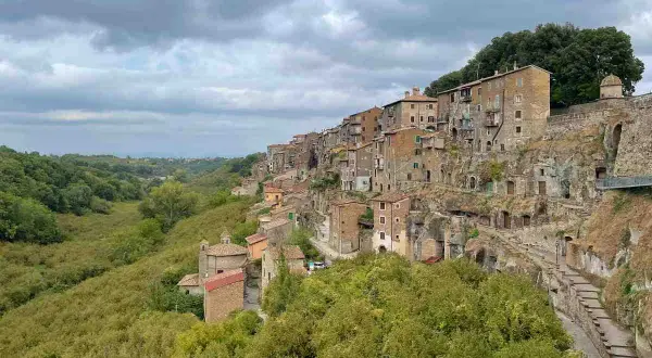 Case aggrappate alla roccia, un borgo pittoresco vicino al lago di Vico, con una valle verdeggiante.