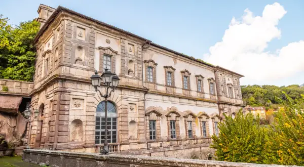 Il **Palazzo Chigi Soriano nel Cimino**, con la sua facciata imponente e le finestre eleganti, si staglia contro un cielo azzurro con nuvole bianche.