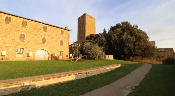 Antica torre di lavello tuscania, con edifici in pietra e un sentiero nel prato sotto un cielo azzurro.