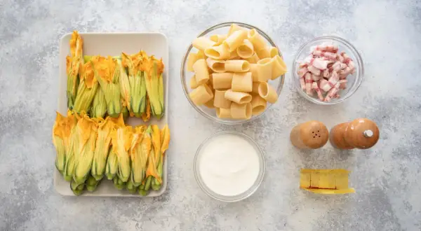 Fiori di zucca freschi, rigatoni, guanciale a cubetti, panna, sale, pepe e un pezzo di formaggio. Ingredienti per un piatto gustoso.