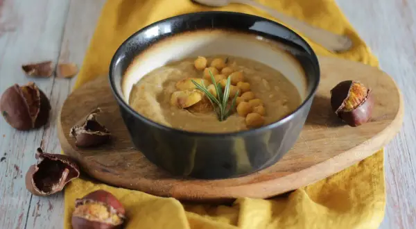 Una ciotola di zuppa ceci e castagne viterbese, guarnita con ceci, castagne e rosmarino, circondata da castagne.