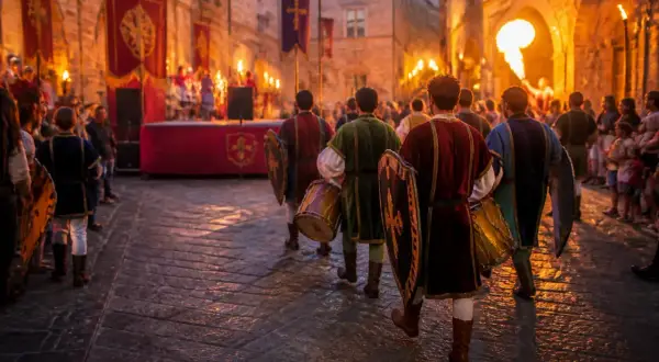 Uomini in costume d'epoca sfilano con tamburi e scudi, creando un'atmosfera di rievocazione medievale illuminata da torce.