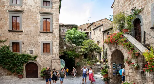 Un vicolo pittoresco nella Tuscia, con case in pietra, fiori colorati e turisti che passeggiano.
