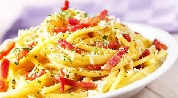 Un piatto fumante di spaghetti alla carbonara, uno dei secondi piatti tipici del Lazio, con guanciale croccante, pecorino romano e prezzemolo tritato.
