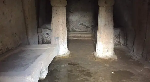 Interno di una tomba a dado scavata nella roccia, con un sarcofago in pietra e colonne grezze.