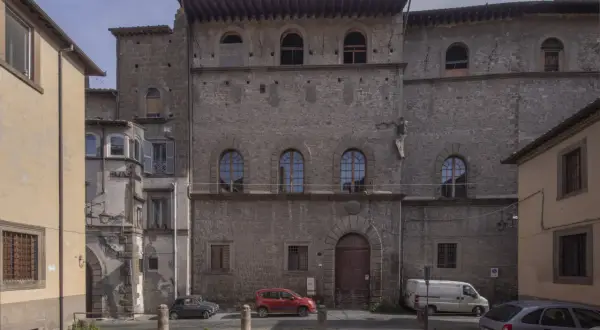 Antico palazzo chigi viterbo con finestre ad arco e un portone in legno. Auto parcheggiate nella piazza antistante.