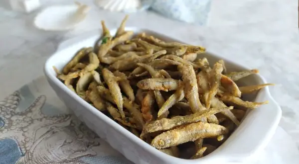 Un piatto bianco pieno di lattarini pesce fritti, croccanti e dorati, con un tocco di prezzemolo.