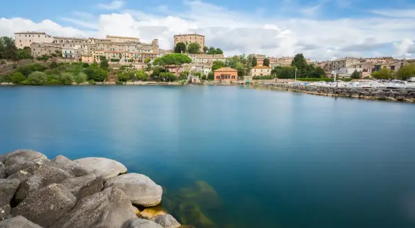 Vista del lago di Bolsena con il borgo in lontananza. Il diametro del lago di Bolsena è imponente, con acque calme e rocce in primo piano.