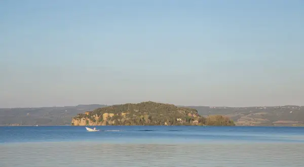 Un'isola Martana verdeggiante si staglia sul lago azzurro, con una barca bianca che solca le acque calme.
