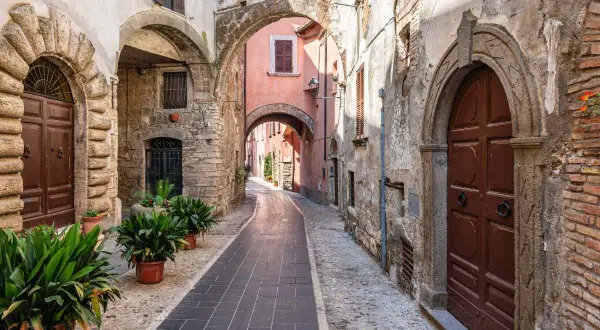 Un vicolo suggestivo a Orte, Viterbo, con archi in pietra, porte antiche e piante verdi.
