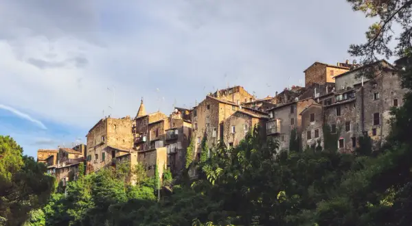 Antiche case in pietra si aggrappano alla collina a Capranica, Viterbo, con vegetazione lussureggiante che le circonda.