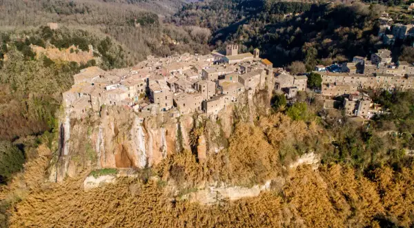 Antico borgo di Calcata Viterbo arroccato su una rupe tufacea, circondato da vegetazione secca e boschi.