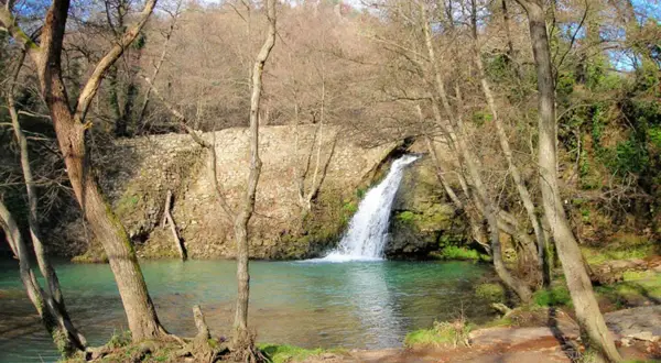 Cascata della mola di Oriolo, con acque turchesi e alberi spogli che incorniciano la scena.