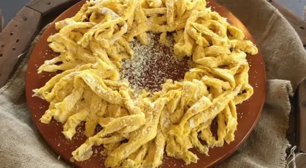 Frittelloni di Civita Castellana, pasta fresca fatta in casa, cosparsa di formaggio grattugiato, disposta a corona su un piatto di terracotta.