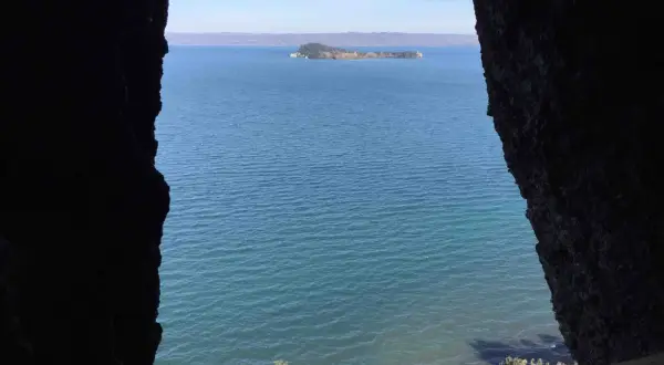 Vista da una grotta sul lago, con un'isola verde in lontananza. Il **monte Bisenzio** si staglia all'orizzonte.