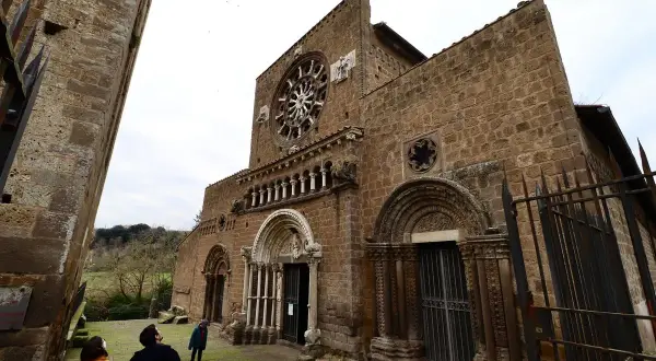 La facciata romanica di Santa Maria Maggiore a Tuscania, con il suo rosone e i portali scolpiti, vista da un angolo con visitatori che ammirano la struttura.