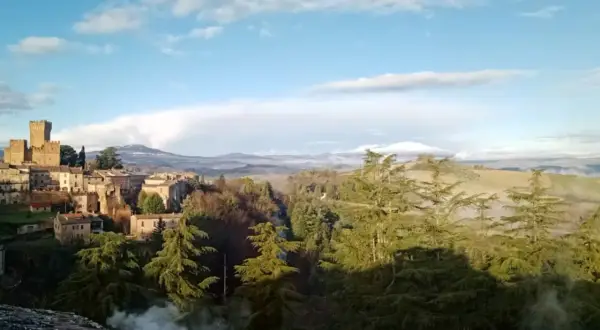 Borgo medievale con torre imponente, immerso nel verde del comune di Proceno, con colline nebbiose all'orizzonte.