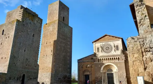 Le chiese di Tuscania, con le loro torri medievali e la facciata romanica, si stagliano contro un cielo azzurro.