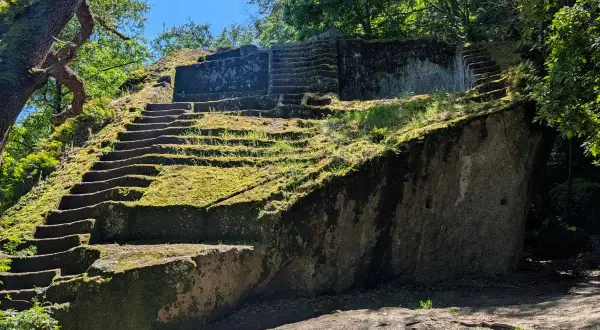 Antica piramide etrusca scavata nella roccia, ricoperta di muschio e circondata da alberi secolari.