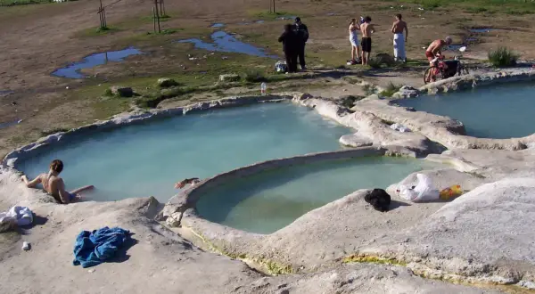 Persone si rilassano nelle acque termali del lago Viterbo, con un paesaggio rurale sullo sfondo.