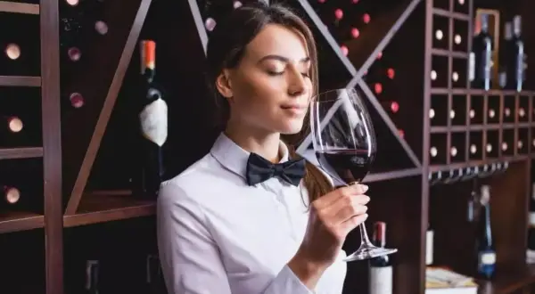 Sommelier annusa un bicchiere di vino Cannaiola, circondata da scaffali pieni di bottiglie.