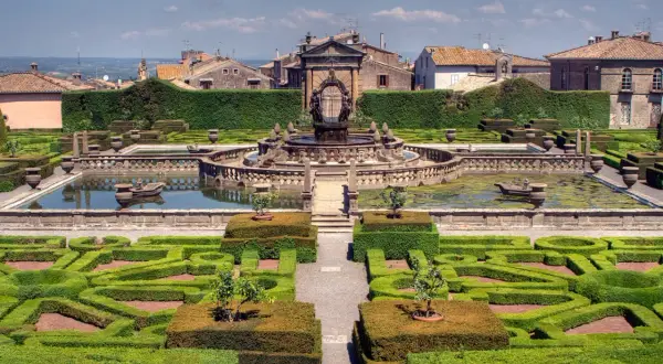 Giardini all'italiana con fontana centrale e siepi geometriche. Si vede il borgo di Bagnaia sullo sfondo.
