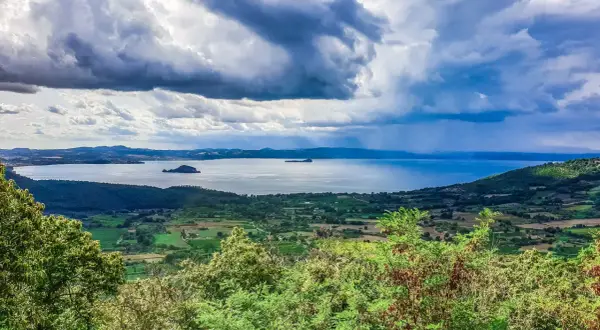 Vista panoramica del lago di Bolsena con isole, colline verdi e un cielo drammatico. Un paesaggio mozzafiato da Capodimonte.