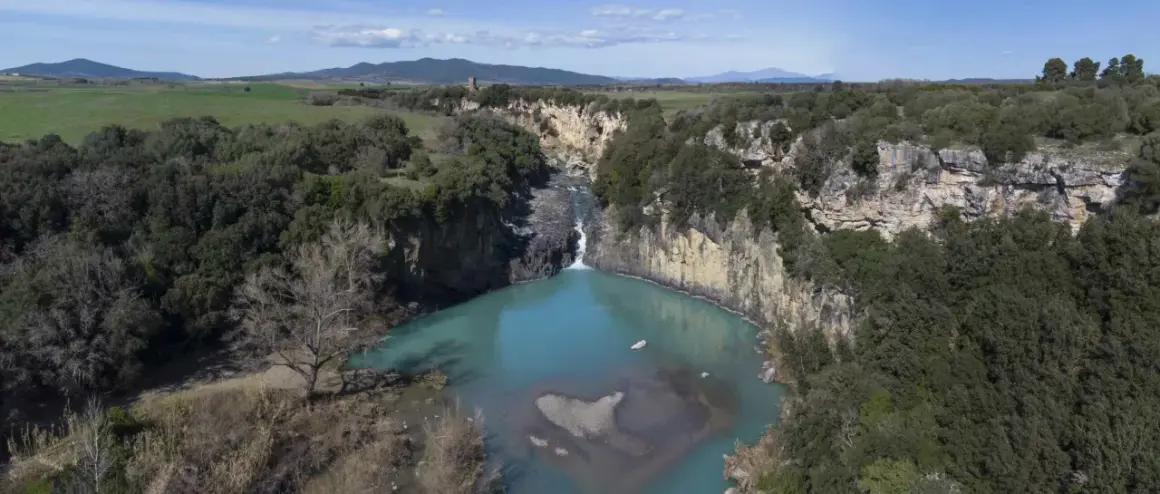 Cascata del Pelago, un gioiello naturale dove si trova Vulci, con acque turchesi che si infrangono tra rocce e vegetazione lussureggiante.