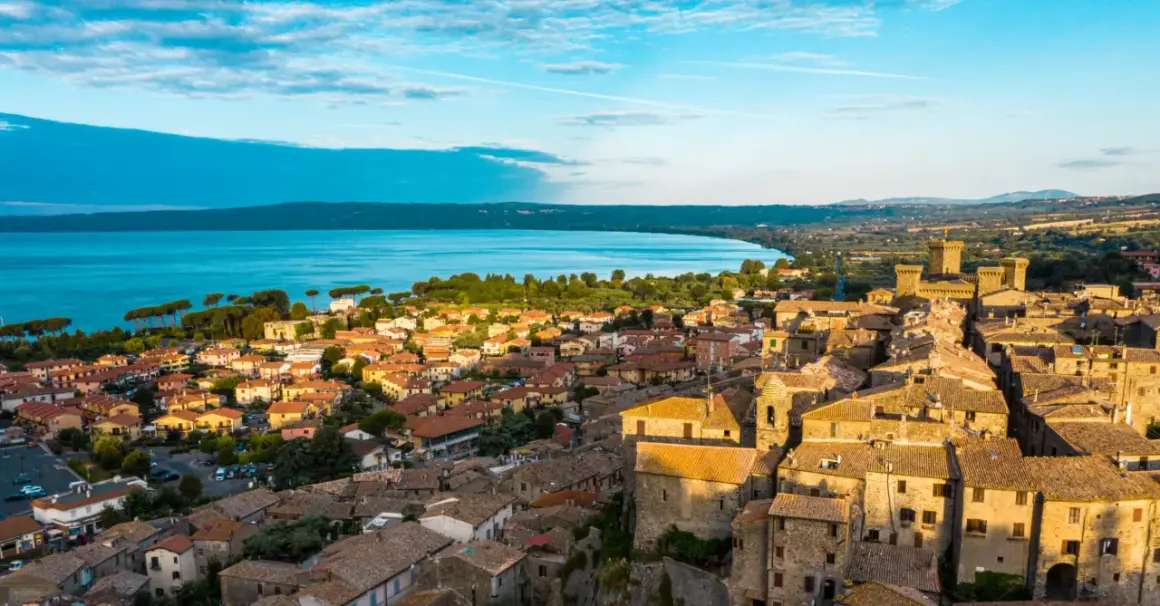 Borghi da visitare vicino Bolsena: vista aerea di un antico castello e case con tetti in tegole rosse, con il lago sullo sfondo.