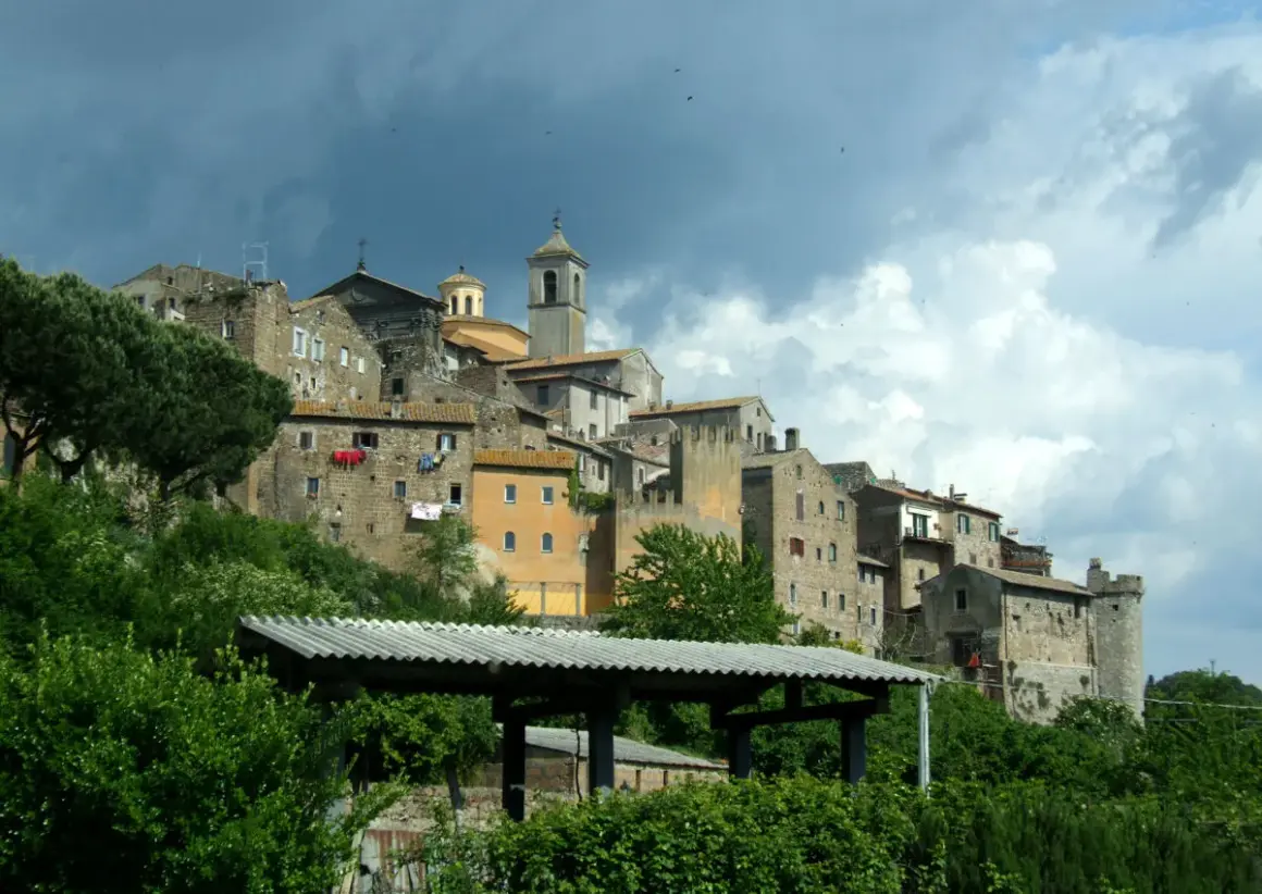 Antico borgo di **Tuscie Vetralla**, con case in pietra aggrappate alla collina sotto un cielo nuvoloso.