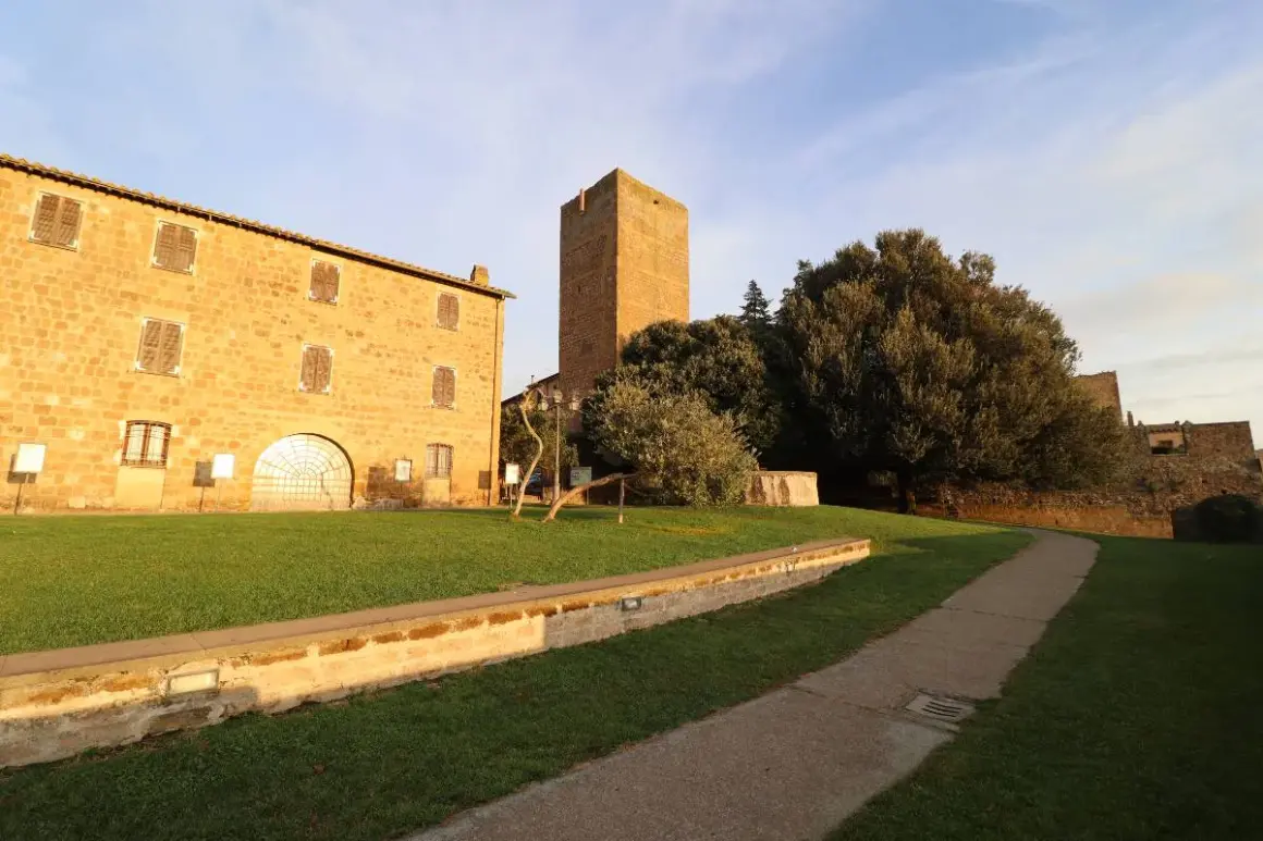 Antica torre di lavello tuscania, con edifici in pietra e un sentiero nel prato sotto un cielo azzurro.