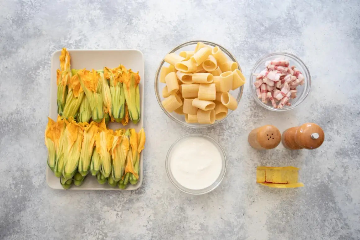 Fiori di zucca freschi, rigatoni, guanciale a cubetti, panna, sale, pepe e un pezzo di formaggio. Ingredienti per un piatto gustoso.