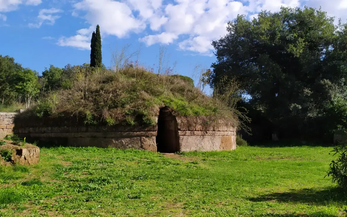 Antica tomba etrusca nel Lazio, con un ingresso ad arco e un tumulo ricoperto di vegetazione.