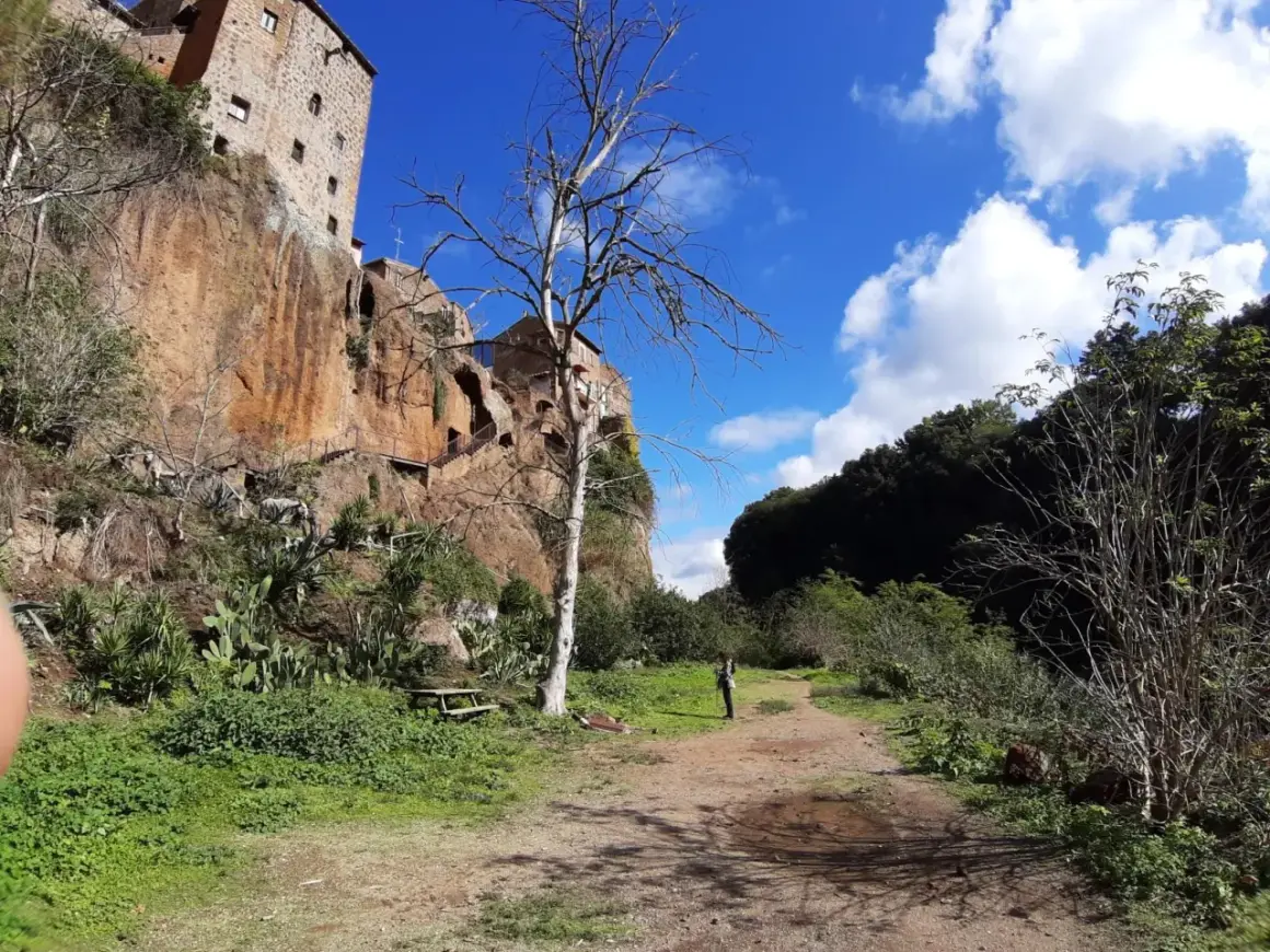 Sentiero verso Castel Sant'Elia, cosa vedere: roccia imponente, vegetazione rigogliosa e un cielo azzurro con nuvole bianche.