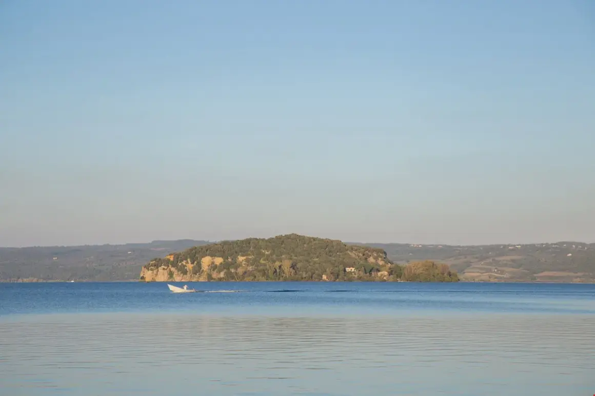 Un'isola Martana verdeggiante si staglia sul lago azzurro, con una barca bianca che solca le acque calme.
