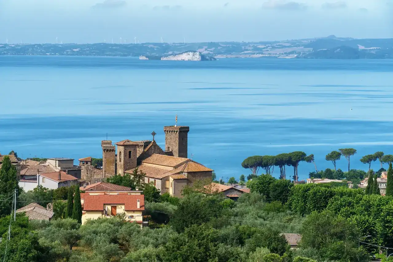 Borgo medievale con castello affacciato sul lago, tra ulivi e pini. Immagina un bicchiere di vino Cannaiola in questo paesaggio.