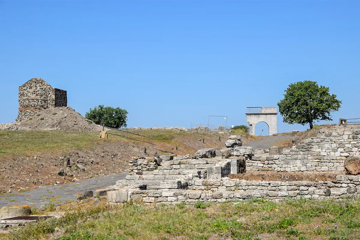 Rovine antiche a Montalto di Castro, con un rudere a sinistra e un arco moderno a destra, sotto un cielo azzurro.