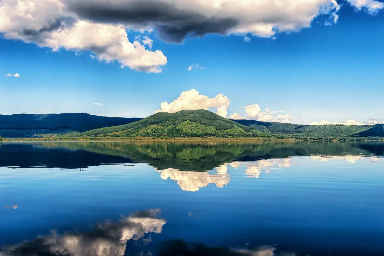 Un lago calmo riflette colline verdi e nuvole bianche. Una vista incantevole del bella Venere lago di Vico.