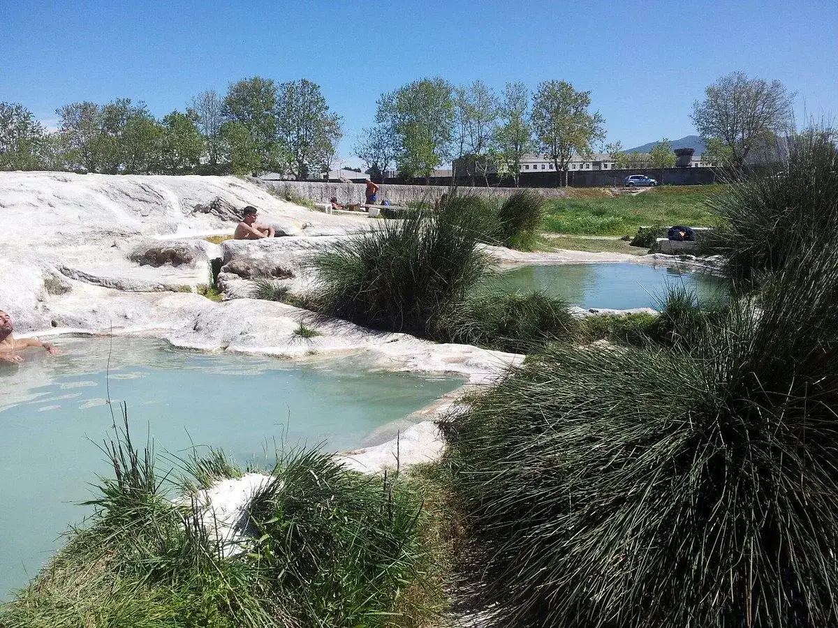 Persone rilassate nelle acque azzurre delle terme di San Sisto, circondate da rocce bianche e vegetazione rigogliosa.