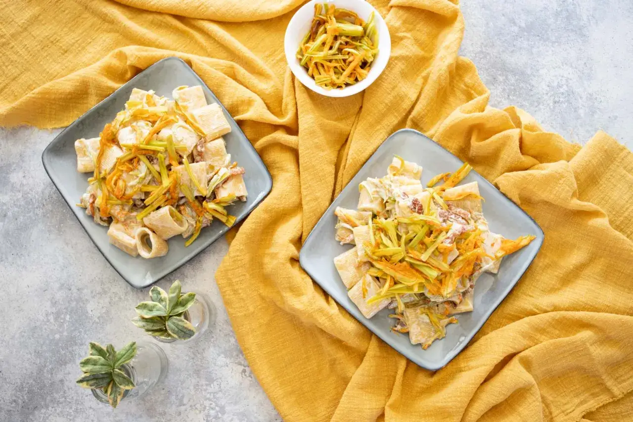Due piatti di paccheri conditi con fiori di zucca e guanciale croccante, su un tovagliolo giallo.