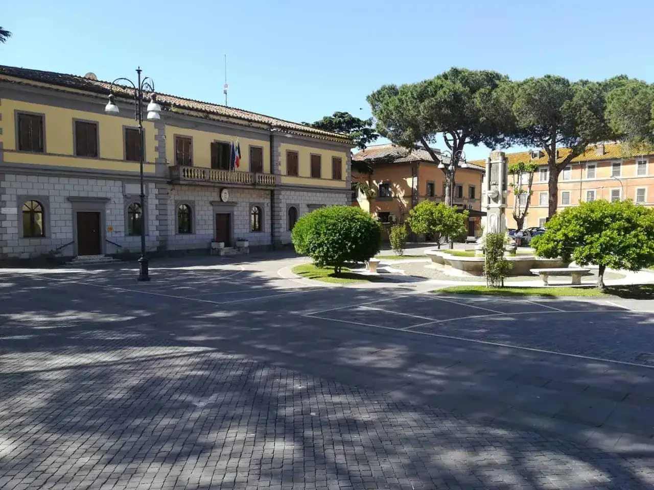 Piazza del Municipio a Monte Romano, Viterbo, con fontana, alberi e il palazzo comunale.