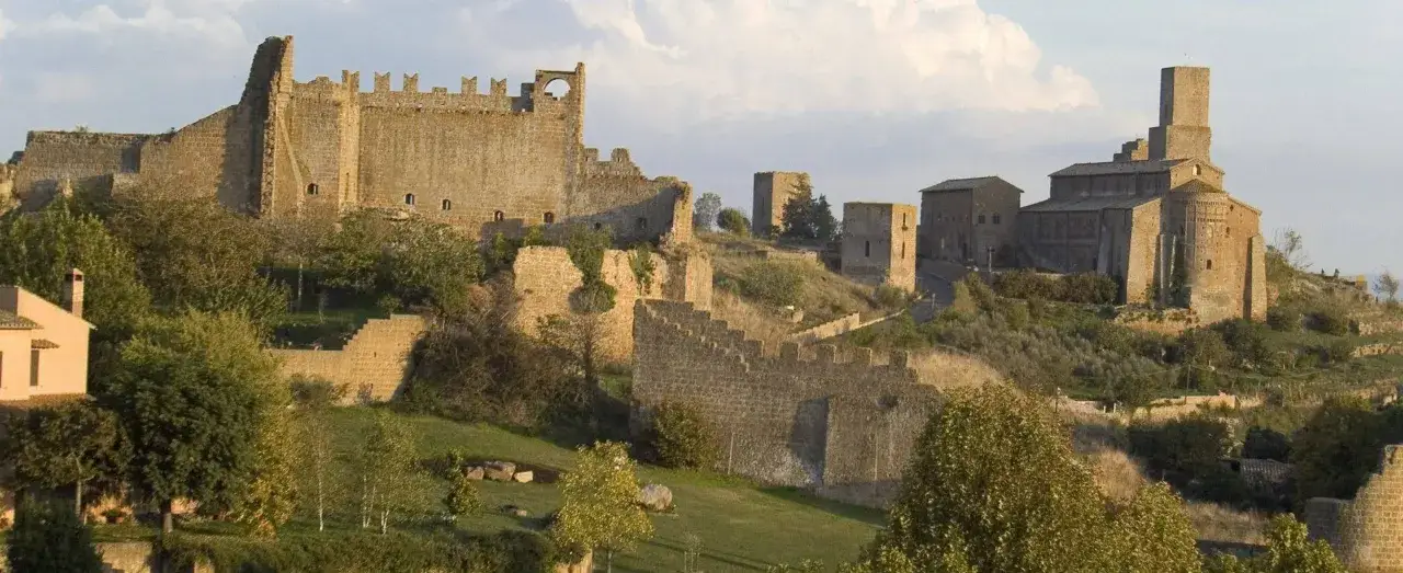 Antico borgo fortificato di Tuscania (VT) con rovine di mura e torri, e una chiesa imponente sulla collina.
