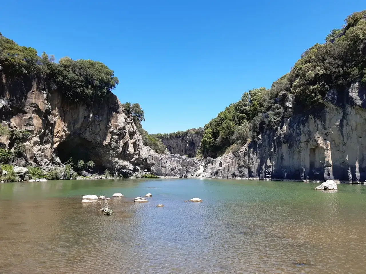 Il lago di Vulci, incastonato tra imponenti pareti rocciose ricoperte di vegetazione, riflette il cielo azzurro.